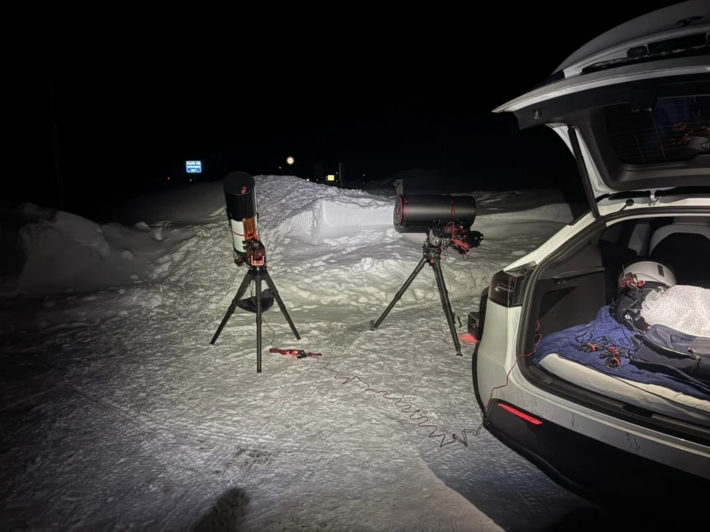 Telescopes set up beside a car on a snowy mountain observing night