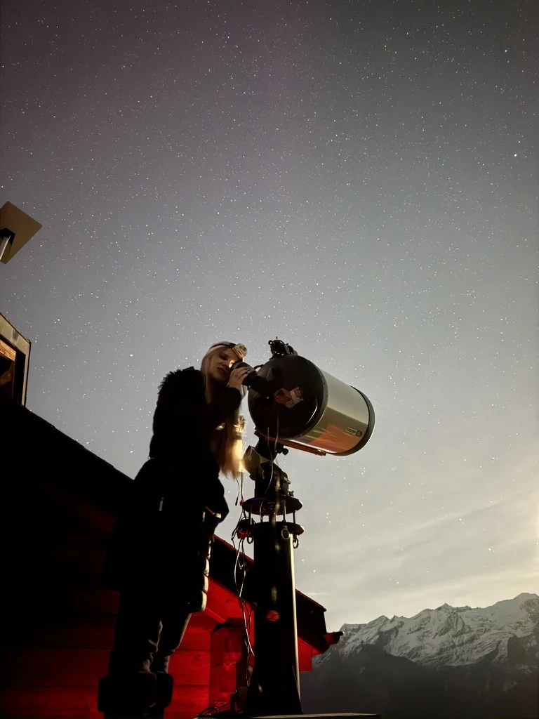 Luca looking into a large telescope under a starry Alpine night sky