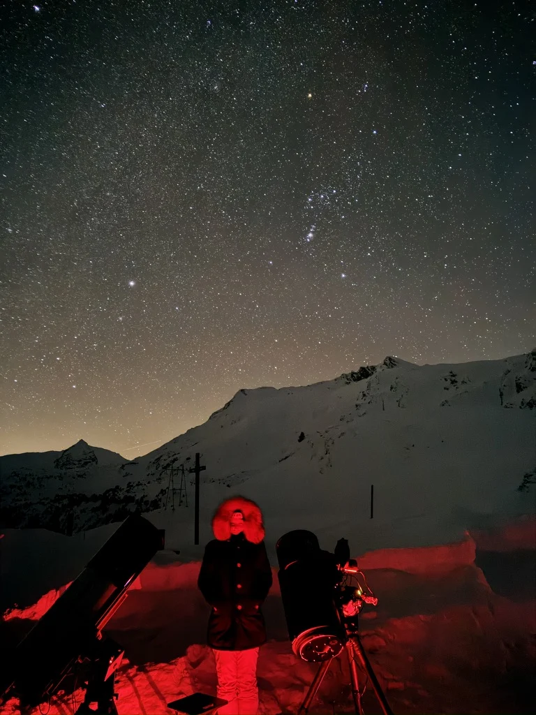Luca standing between telescopes at a snowy Alpine observing site under a starry sky