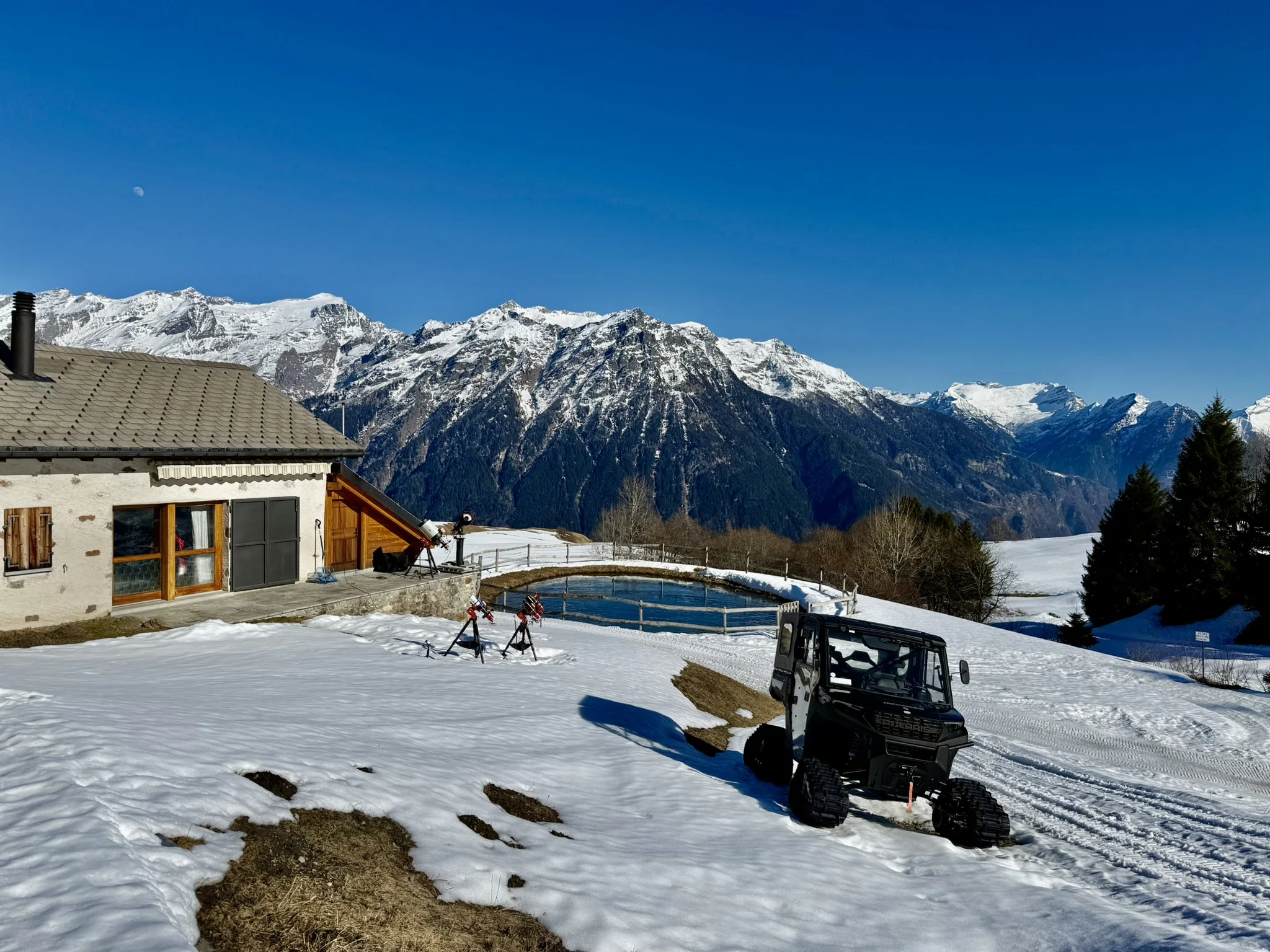 Snowy mountain observing location with a small Alpine chalet under a dark sky