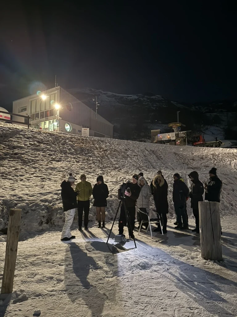 People gathered around a telescope during a snowy mountain outreach session at night