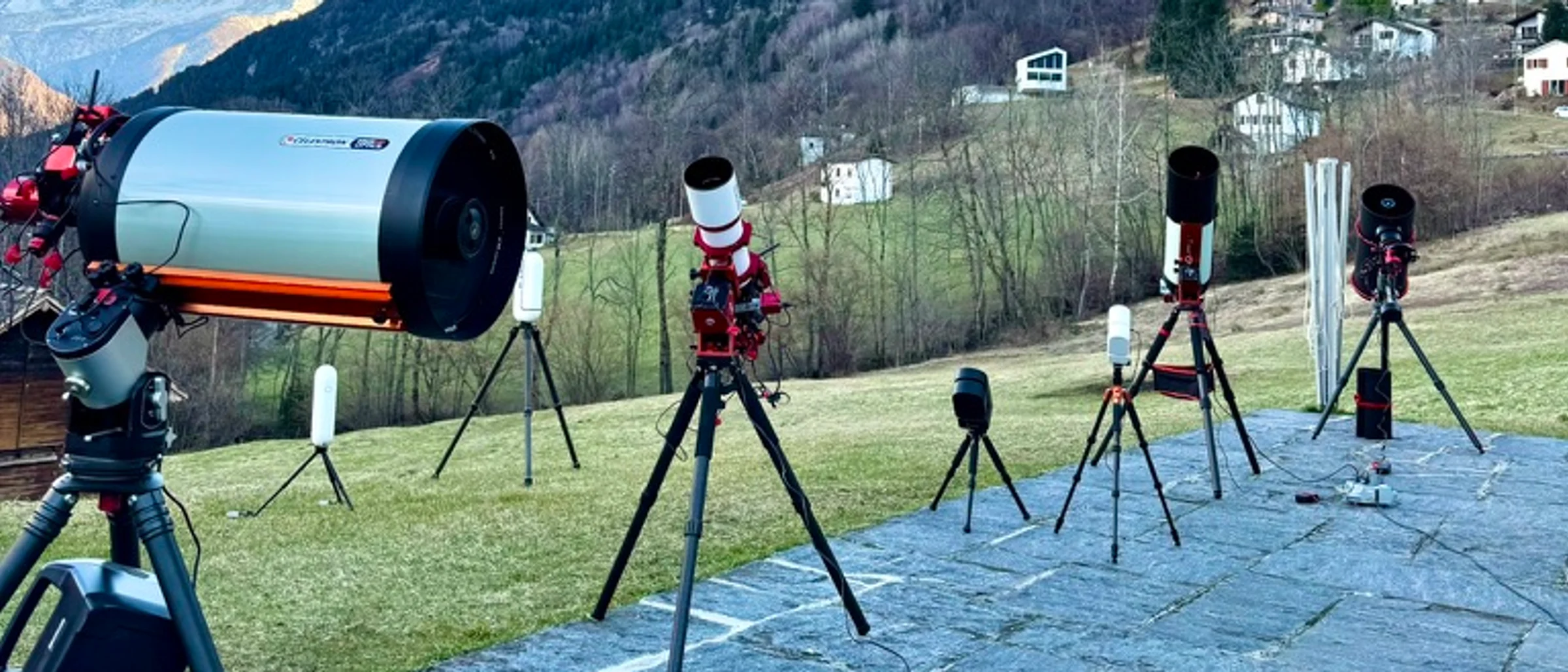 Astrophotography telescopes set up on an Alpine terrace in front of mountain peaks